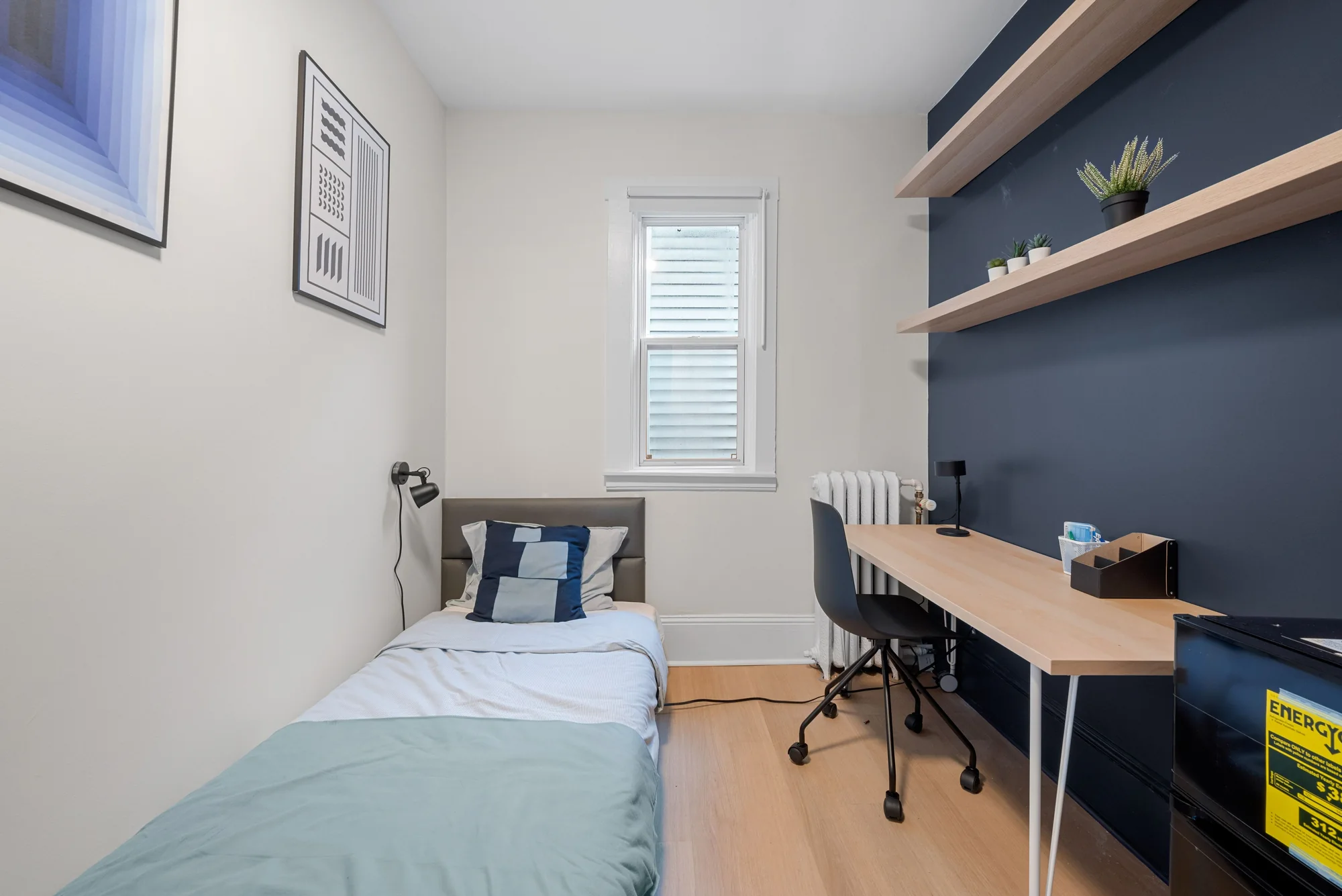 Narrow room example with tall window, bed, and blue desk
